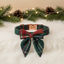 Green plaid dog collar with bow tie on a white surface with Christmas decorations in the background